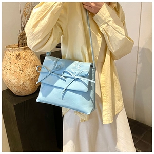 Light blue crossbody bag featuring pleated texture and bow detail on flap shown on model