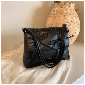 Detail of black faux leather tote bag with bow design and white fashion lettering