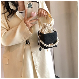 Détail du sac seau cube avec motif croco noir et poignée perlée sur costume blanc