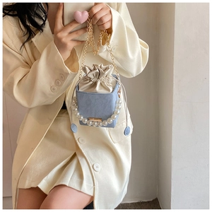 Gros plan sur un sac seau en PU bleu clair avec poignée en perles et chaîne dorée