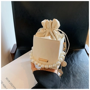 Détail du sac seau blanc avec anse en perles élégantes et bandoulière dorée