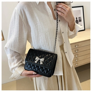 Detail of a quilted crossbody bag with a silver metal bow buckle and chain strap