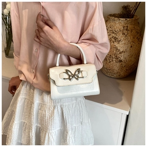 Detail of white glossy patent leather handbag featuring a silver butterfly clasp and handle
