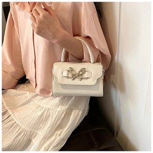 Detail of cream white glossy leather handbag featuring a decorative metal butterfly clasp