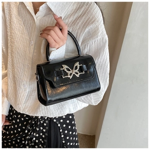 Detail of black glossy handbag featuring a silver butterfly clasp and structured top handle