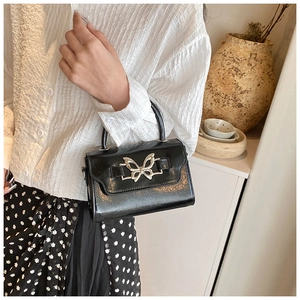 Detail of elegant black glossy leather handbag with a decorative silver butterfly clasp