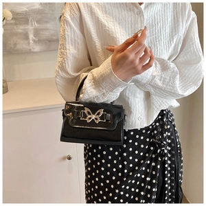 Detail of black patent leather mini handbag with a silver butterfly buckle closure