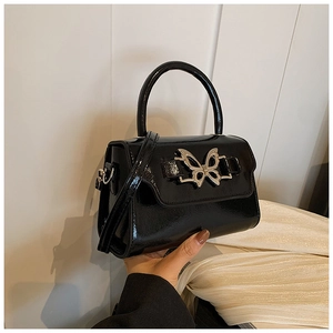 Close-up of black patent leather mini bag featuring a silver metal butterfly buckle