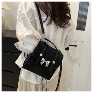 Detail of black suede mini backpack featuring a silver butterfly bow and versatile shoulder strap