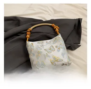 Detail of white satin bag with colorful butterfly embroidery and round wooden bead handle