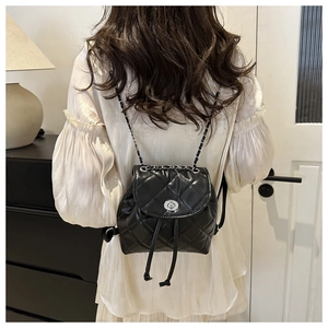 Detail of a black quilted leather mini backpack with silver chain straps and turn-lock