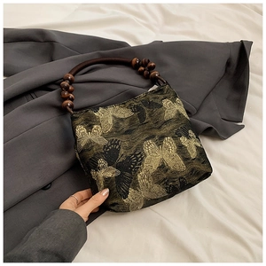 Close-up of golden butterfly embroidery and dark wooden bead handle on a black tote bag