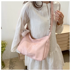 Sac bandoulière demi-lune en velours rose avec breloque ours dans un décor chaleureux