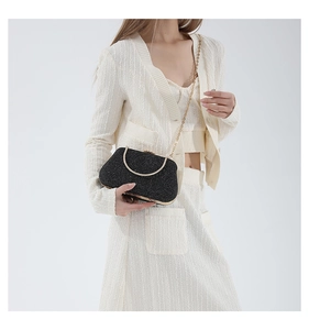 Detail of black sequined evening bag with golden circular handle and chain strap on model