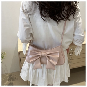 Detail of light pink crossbody bag with large bow decoration worn by a model