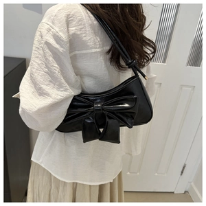 Side view of black glossy shoulder bag with large bow detail worn by a model
