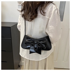 Elegante borsa a spalla in vernice nera con grande fiocco decorativo indossata dal modello