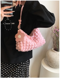 Detail of pink ruched fabric handbag featuring a delicate floral charm and slim strap