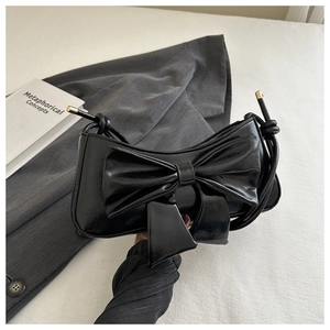 Elegante borsa a spalla in vernice nera con fiocco grande su sfondo minimalista