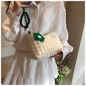 Detail of white pleated cloud bag with green flower charm and black beaded handle strap