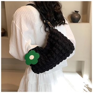 Detailed texture of black bubble pleated shoulder bag with a green floral charm
