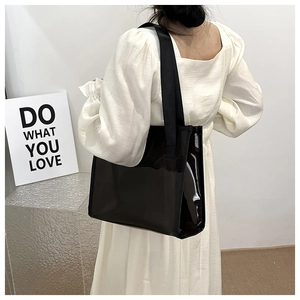 Detail of minimalist black patent leather tote bag with wide strap on model shoulder