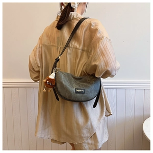 Detail of grey dumpling bag with adjustable strap and a cute plush doll pendant accessory