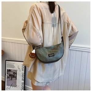 Detail of dark green canvas crescent bag with a plush charm and adjustable strap
