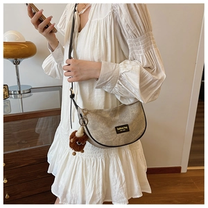 Detail of beige textured crescent bag with New York leather patch and plush monster charm