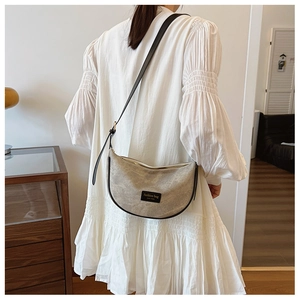 Detailed side view of beige crescent bag with black leather trim and woven strap