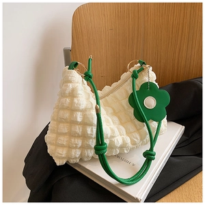 Detail of white pleated bag with green knotted shoulder strap and floral charm accessory