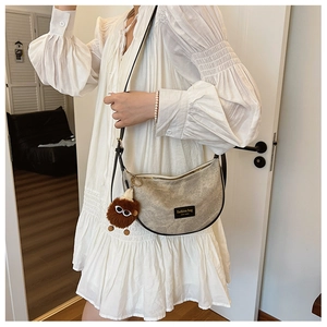 Detail of grey crescent shoulder bag with vintage texture and cute plush monster charm