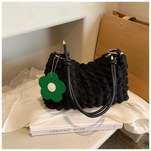 Close-up of black bubble textured cloud bag with green flower charm and gold hardware