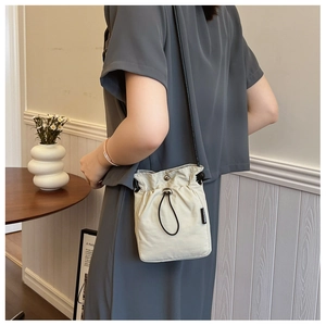 Detail of a beige drawstring crossbody bag with fashion label on a soft nylon surface