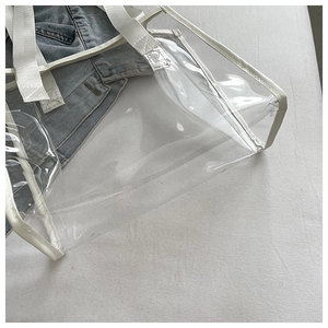 Detailed close-up of transparent PVC tote bag featuring white fabric handles and leather trim