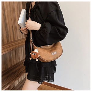 Close-up of brown PU leather crescent bag with plush charm on a black lace dress