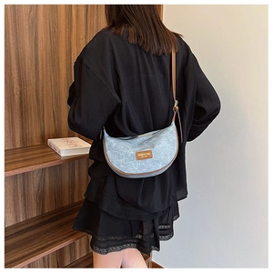 Detail of denim-style crescent crossbody bag with brown leather trim shown on shoulder