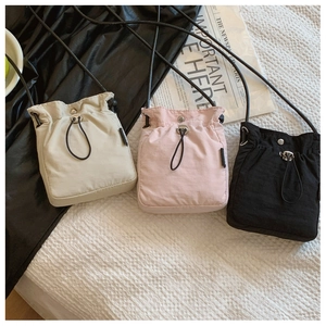 Close-up of lightweight nylon crossbody bags with drawstrings in white, pink, and black