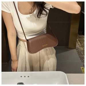 Détail du sac sous le bras marron foncé à motif crocodile avec logo doré et bandoulière