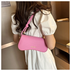 Détail d'un sac bandoulière rose texture crocodile avec nœud stylé sur une robe blanche