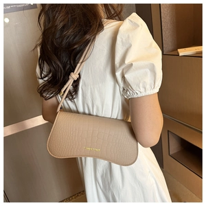 Détail d'un sac à bandoulière beige à relief crocodile avec base ondulée et bandoulière nouée