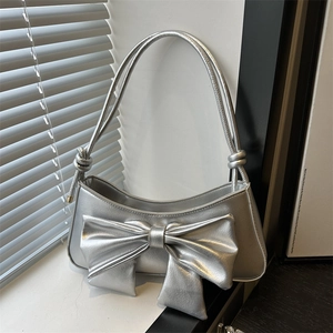 Silver metallic shoulder bag with large bow and knots displayed on a white windowsill