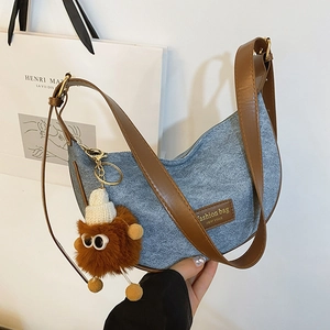 Blue denim crescent shoulder bag with brown leather strap and plush monster charm decoration