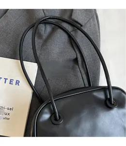 Detail of black glossy leather tote bag showing round metallic eyelets and long shoulder strap