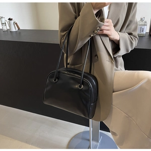 Detail view of black matte leather tote bag featuring a smooth zip closure and slender handles
