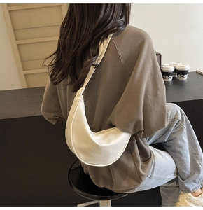 Modèle portant un sac demi-lune en nylon crème montrant le détail de la bandoulière large
