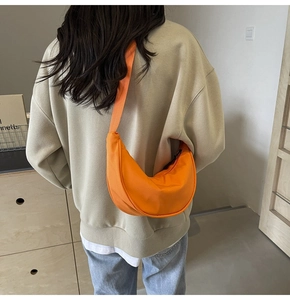 Détail du sac demi-lune en nylon orange avec bandoulière réglable porté par un modèle