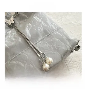 Détail du sac seau argenté avec breloque papillon en métal et cordons de serrage en perles