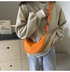 Détail d'un sac bandoulière demi-lune en nylon orange porté par un mannequin en intérieur