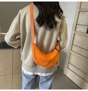Détail d'un sac bandoulière orange en nylon en forme de croissant porté par un mannequin